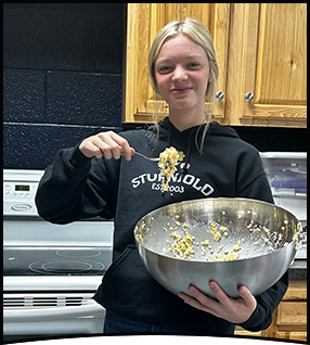 Happy female student holding a huge metal bowl in the kitchen
